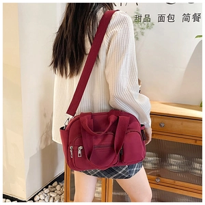 Side view of burgundy nylon Boston bag with multiple zippers and wide fabric strap
