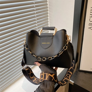 Black bucket bag with gold handle, chain decor and patterned strap in urban setting