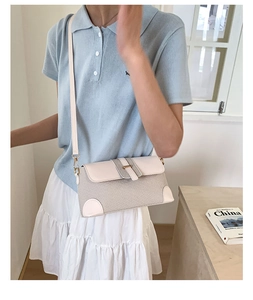 Detail of cream leather and woven texture baguette bag on model with blue polo shirt