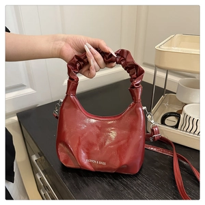 Macro view of burgundy glossy leather handbag with artistic pleated handle and white text