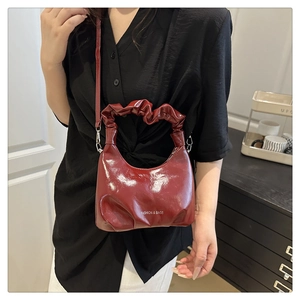 Close-up of wine red glossy handbag featuring trendy ruched handle and silver hardware