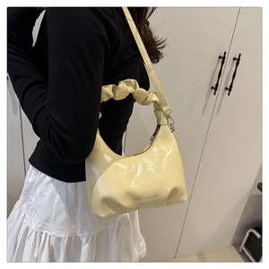 Detail of cream yellow hobo bag with pleated handle and polished patent leather texture