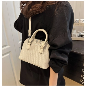 Detail of a creamy beige shell-shaped handbag with crocodile texture and fashion logo