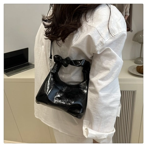 Detail of black glossy crescent bag with pleated handle worn by a model in a casual setting