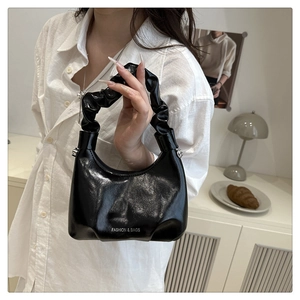 Detail of the pleated cloud handle on the black glossy leather shoulder bag