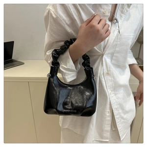 Detail of black shiny leather hobo bag with unique gathered handle and letter print