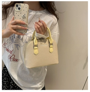 Model holding beige woven shell bag with yellow leather trim and dual metal zippers