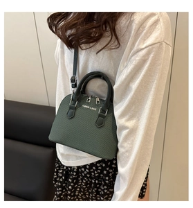 Close-up of a dark green shell bag with woven texture, black handles and metal zippers