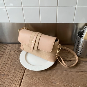 Détail d'un sac beige en similicuir et tissage avec barre dorée et fine bandoulière chic