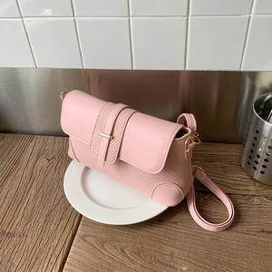 Sac bandoulière rose pâle avec texture contrastée et boucle dorée sur une assiette