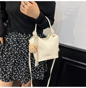 Detail of cream bucket bag with knot handle, floral dress styling, and plush bear charm