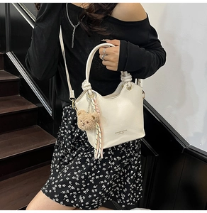 Chic beige bucket bag with plush bear charm and striped tassel shown on shoulder