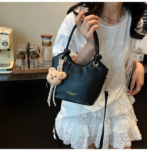 Detail of black leather bucket bag with cute brown bear charm and golden lettering