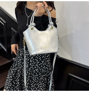 Close-up of metallic silver bucket bag with knotted handle and golden brand logo detail