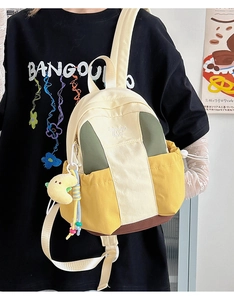 Close-up of color-block canvas backpack with brand embroidery and plush moon charm detail