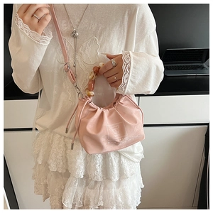 Pink pleated crossbody bag with amber bead handle and bear graphic shown on model