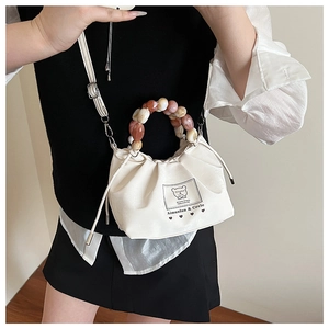 Close-up of white crossbody bag with marble bead handle and bear logo print details