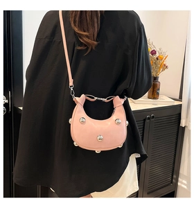 Pink crescent shoulder bag with polished silver studs shown against a black outfit