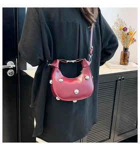 Sac bandoulière en demi-lune rouge foncé avec clous argentés porté par un modèle