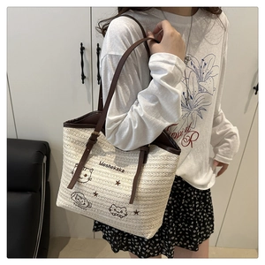 Detail of woven straw tote bag featuring cute cat embroidery and brown leather straps