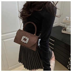 Détail d'un mini sac en daim marron foncé avec boucle en cristal et bandoulière en chaîne