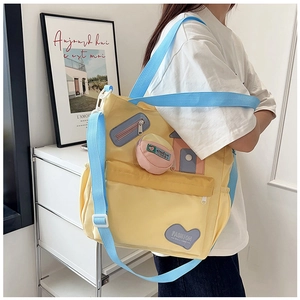 Detail of yellow canvas crossbody bag featuring blue strap and heart shaped fashion patch