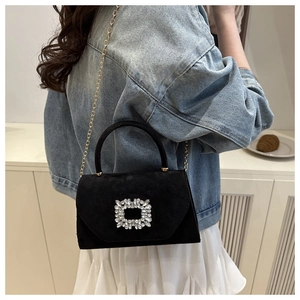 Detailed view of a black suede square handbag featuring a large sparkling rhinestone buckle