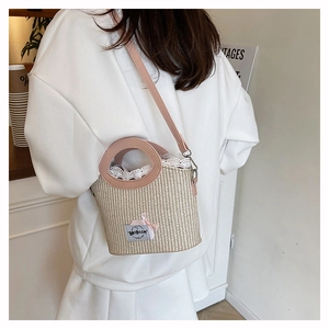 Détail du sac seau en paille avec dentelle blanche et bandoulière en cuir rose