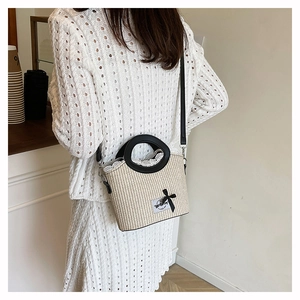 Detail of a straw tote bag featuring white lace trim, black bow, and leather handles