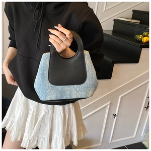 Detail showing the contrast of blue denim and black leather handles on a bucket bag