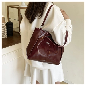 Detail of burgundy glossy patent leather tote bag with silver metal bow and long straps