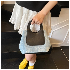 Detail of blue denim bucket bag with black leather handle shown in casual lifestyle use
