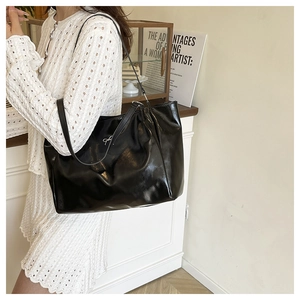 Side view of large black patent leather tote bag with silver bow detail on model