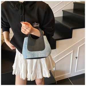 Fashionable mini handbag featuring blue denim and black leather patchwork on model