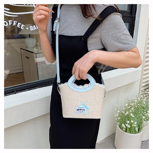 Detail of straw bucket bag with blue leather trim and delicate ribbon bow accessory