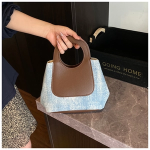 Detail of blue denim bucket bag with brown leather handles held by a model