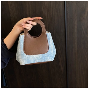Detail of blue denim fabric and brown leather handle on a mini bucket bag