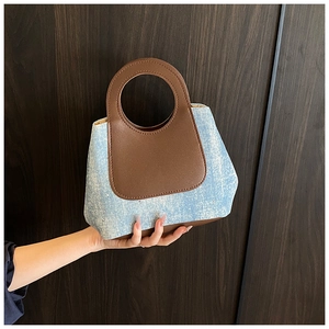 Close-up of contrast denim bucket bag with blue texture and brown leather handle