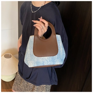 Detail of light blue denim handbag with brown leather base and unique circular handle