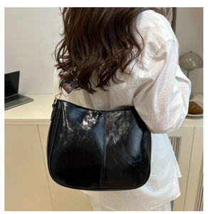 Detail of black patent leather hobo bag with colorful wide strap on a model's shoulder