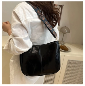 Glossy black shoulder bag featuring a wide bohemian style embroidered guitar strap
