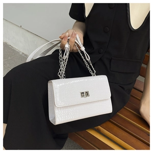 Close-up of white crocodile pattern handbag featuring a silver twist lock and chain strap