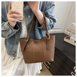 Close-up of brown litchi grain leather texture and fine stitching on a tote handbag