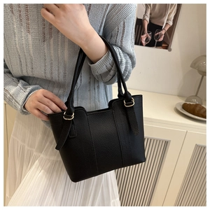 Close-up of black lychee grain leather tote bag with gold metal hardware on model