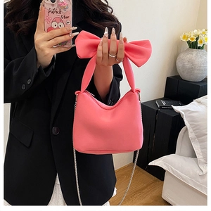 Détail d'un sac à main rose avec nœud et chaîne argentée porté sur un tailleur noir