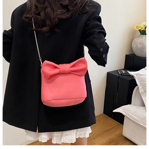 Détail du sac bandoulière rose avec nœud 3D et chaîne argentée sur blazer noir