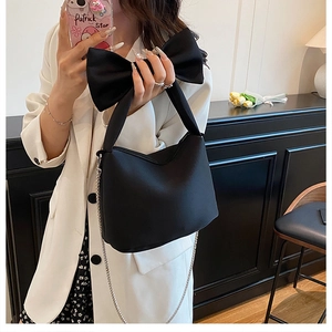 Détail d'un élégant sac à main noir avec un grand nœud et une bandoulière chaîne