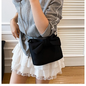 Détail du sac bandoulière noir avec un grand nœud décoratif et une bandoulière chaîne