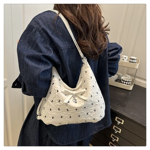 Détail du sac cabas blanc texturé avec motifs noirs, nœud et pendentif en cœur
