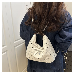 Détail de la texture d'un sac hobo blanc avec nœud décoratif et pendentif cœur
